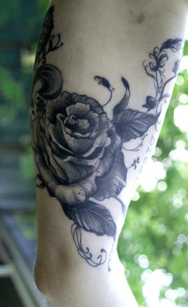 Blackwork rose and dagger tattoo on the forearm.
