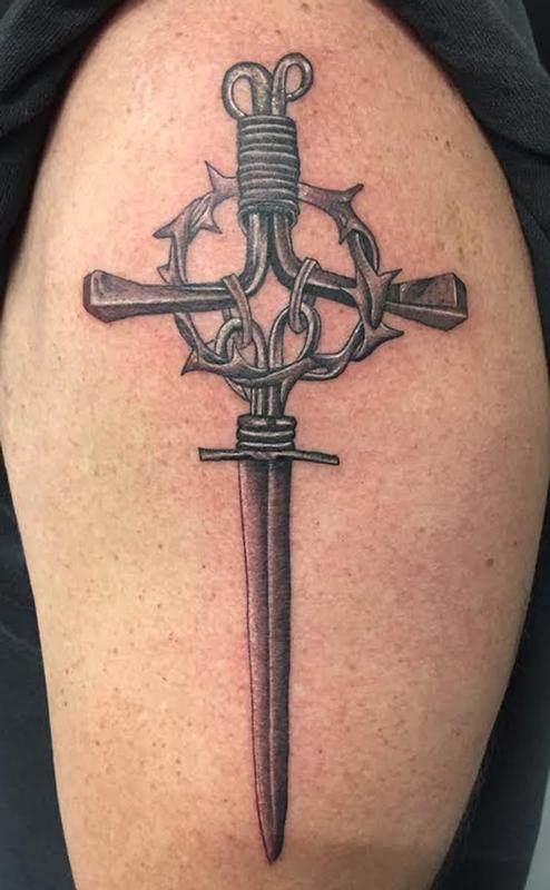 Black shaded cross dagger tattoo on inner lower arm